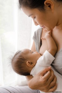 Mother breastfeeding baby, looking down to baby, baby's hand on her shoulder 